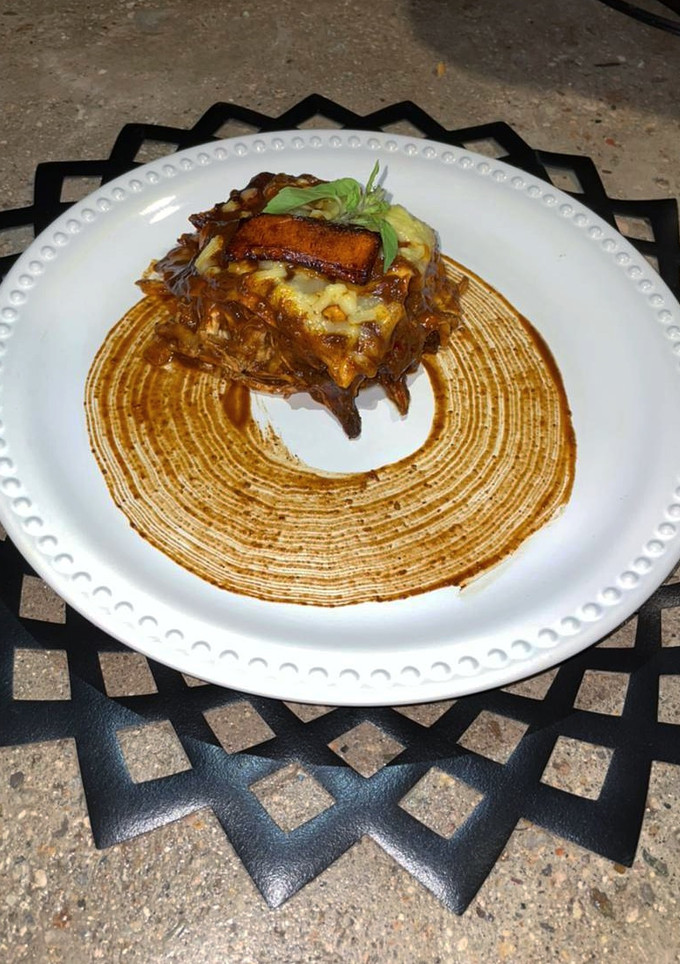 Una foto de Lasaña de mole coloradito con pollo y frituras de plátano macho