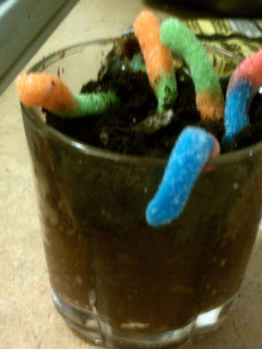 A picture of gummy worms with oreo, and chocolate pudding.