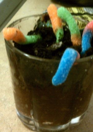 A picture of gummy worms with oreo, and chocolate pudding.