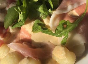 Una foto de Ñoquis con salsa de queso, prosciutto y rúcula