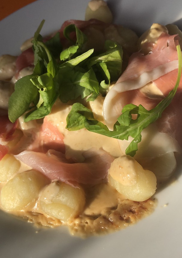 Una foto de Ñoquis con salsa de queso, prosciutto y rúcula