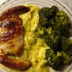 A picture of Pork chops, pork sausages, creamed leeks and steamed broccoli.
