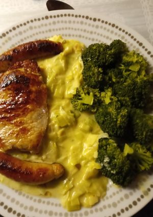 A picture of Pork chops, pork sausages, creamed leeks and steamed broccoli.