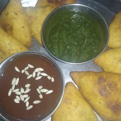 A picture of Aloo samosa with green chutney and imli chutney.