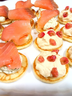 Una foto de Blinis: hummus y granada/queso al eneldo, pistachos y salmón