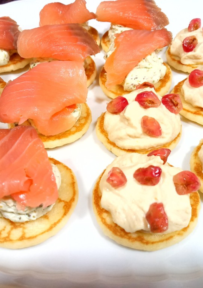 Una foto de Blinis: hummus y granada/queso al eneldo, pistachos y salmón