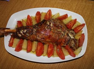 Foto principal de Paletilla de cordero al horno con hierbas aromáticas y guarnición de gajos de patata y tomate asados
