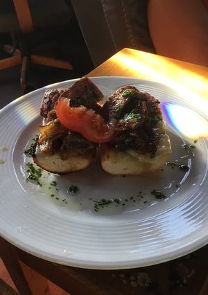 A picture of Open Faced Steak Sandwiches on Garlic Bread with Aged Provolone, Caramelized Onions, and Parsley Oil.