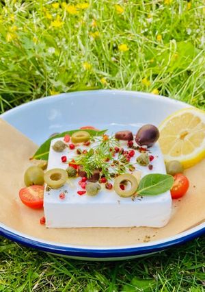 A picture of Baked Vegan Feta with olives, pink peppercorns, lemon and summer herbs and veggies 🌱.