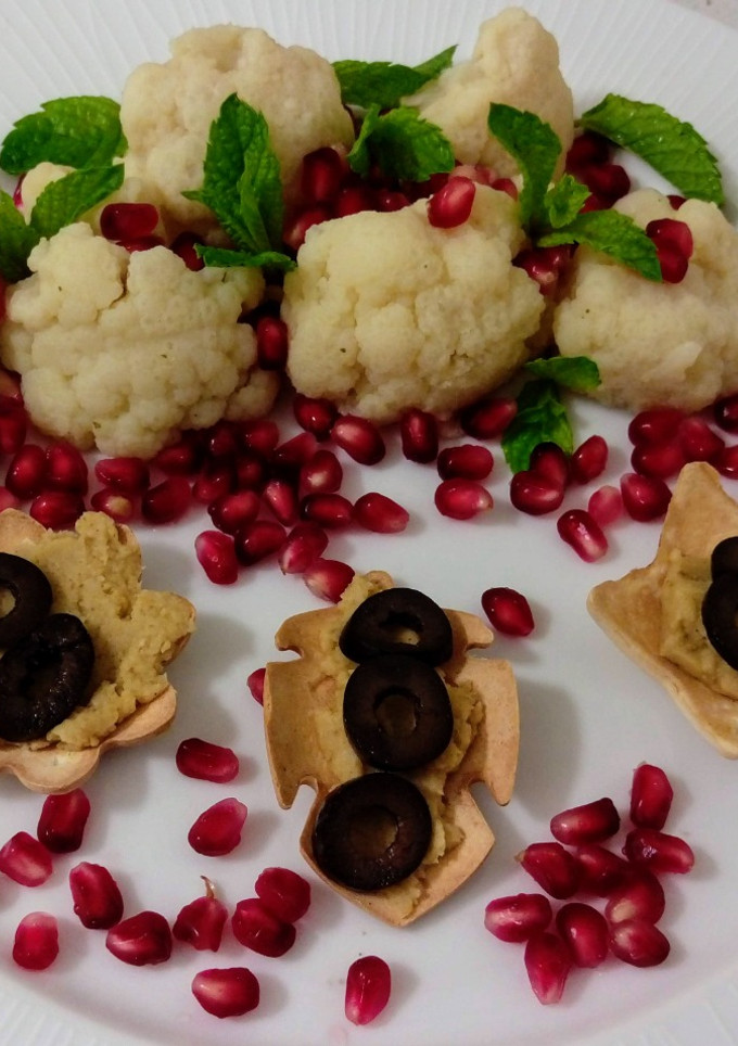 Una foto de Ensalada de coliflor con granada y menta y flores con hummus y aceitunas