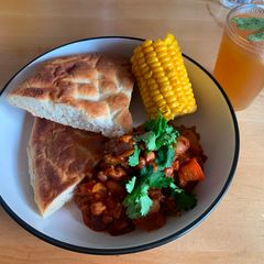 A picture of Five bean chilli with corn on the cob and flatbread.