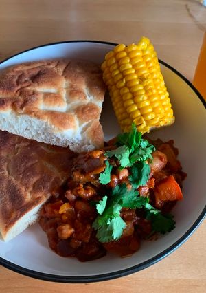 A picture of Five bean chilli with corn on the cob and flatbread.