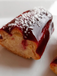 Una foto de Eclair de crema de almendras y cobertura coulis de frutos rojos y coco