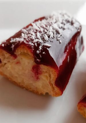Una foto de Eclair de crema de almendras y cobertura coulis de frutos rojos y coco