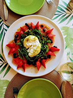Una foto de Capaccio de tomate rosa y fresas con burrata al pesto de almendras sobre nido de rúcula
