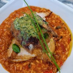 Tomato and chorizo risotto with pan fried chicken supreme and pesto compound A picture of Tomato and chorizo risotto with pan fried chicken supreme and pesto compound.