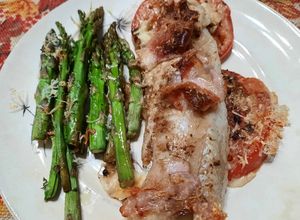 Una foto de Pescado al horno sobre tomates, con espárragos, panceta y hebras de queso