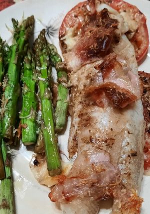 Una foto de Pescado al horno sobre tomates, con espárragos, panceta y hebras de queso