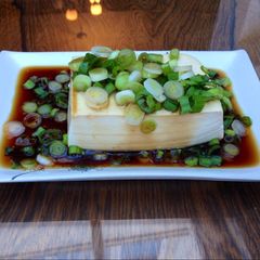 A picture of Steamed tofu with sweet soy dressing sauce and spring onions.