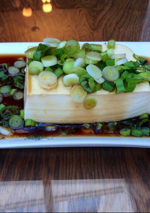 A picture of Steamed tofu with sweet soy dressing sauce and spring onions.