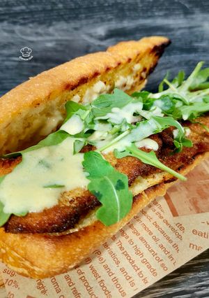 Una foto de Bocadillo de pollo marinado empanado con rúcula y salsa de parmesano