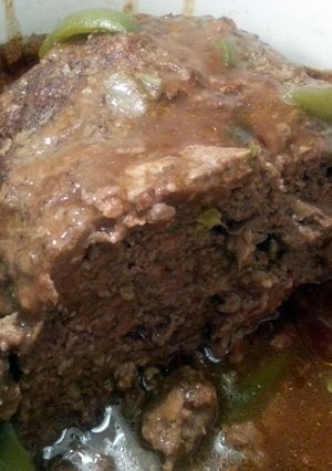 A picture of meatloaf with brown gravy topped with bellpeppers.