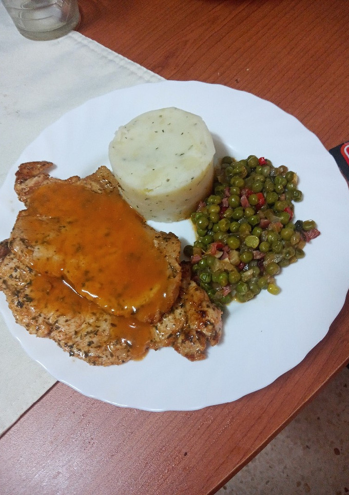 Una foto de Chuletas de cerdo adobadas con puré de papas, guisantes y salsa