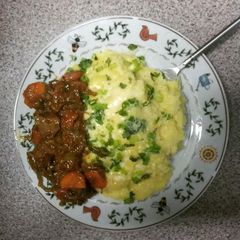 A picture of cheesed mash potatoes topped with spring onions & chicken liver stew.