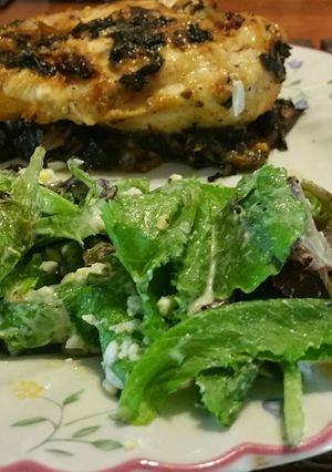 A picture of Chicken breast with baby romaine over bed of spinach.