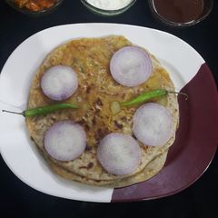A picture of Punjabi Aloo paratha, tamarind chutney, yoghurt and pickle.