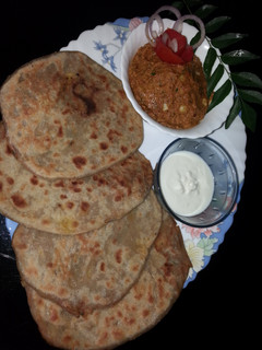 A picture of Aloo paratha with tomato garlic chutney and curd.