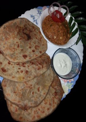 A picture of Aloo paratha with tomato garlic chutney and curd.
