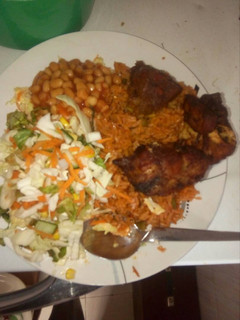 A picture of Jollof rice with salad and chicken,.