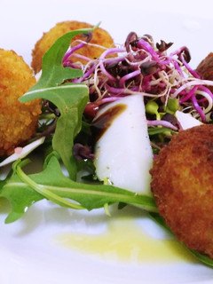 Una foto de Ensalada templada de rúcula y germinados con croquetas de ancas al ajo negro