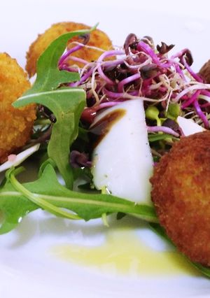 Una foto de Ensalada templada de rúcula y germinados con croquetas de ancas al ajo negro
