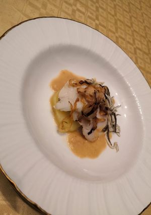 Una foto de Merluza con base de patatas y gulas con salsa de cebolla