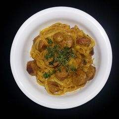 A picture of Rice noodle with curry sauce and sausage.