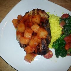 A picture of Grilled center cut pork chop with sweet&sour pineapples, saffron rice and garlic spinach tomato saut.