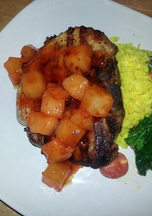 A picture of Grilled center cut pork chop with sweet&sour pineapples, saffron rice and garlic spinach tomato saut.