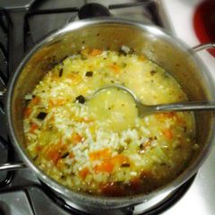 A picture of Risotto rice soup with green zucchini and tomato.