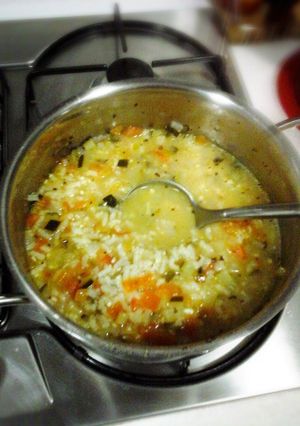A picture of Risotto rice soup with green zucchini and tomato.