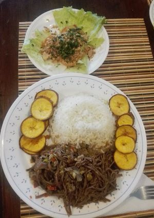 Una foto de Ropa Vieja a mi estilo, acompañada de arroz blanco, monedas de plátano verde con cáscara y ensalada