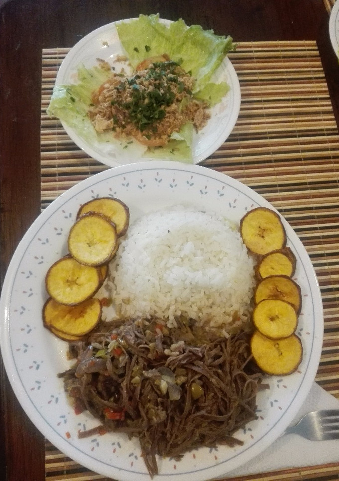 Una foto de Ropa Vieja a mi estilo, acompañada de arroz blanco, monedas de plátano verde con cáscara y ensalada