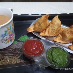 A picture of Samosa with tomato sauce/coriander chutney and tea.
