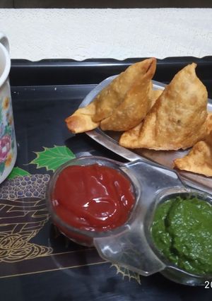 A picture of Samosa with tomato sauce/coriander chutney and tea.