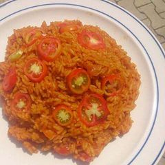 A picture of Jollof rice with fresh sliced tomatoes.