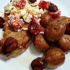 A picture of Baked pork chop, feta, tomato, honey, truffled potatoes & grapes.
