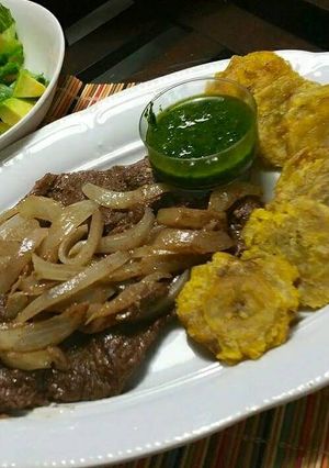 Una foto de Bistec de res encebollado, acompañado con salsa de cilantro.