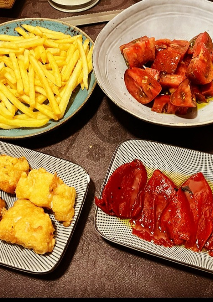 Una foto de Bacalao a la romana, con pimiento caramelizado, patatas caseras y tomate aliñado