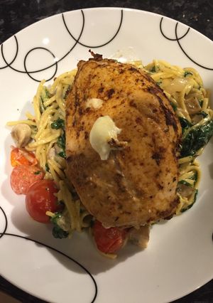 A picture of Stuffed chicken on a bed of creamy cheesy noodles.
